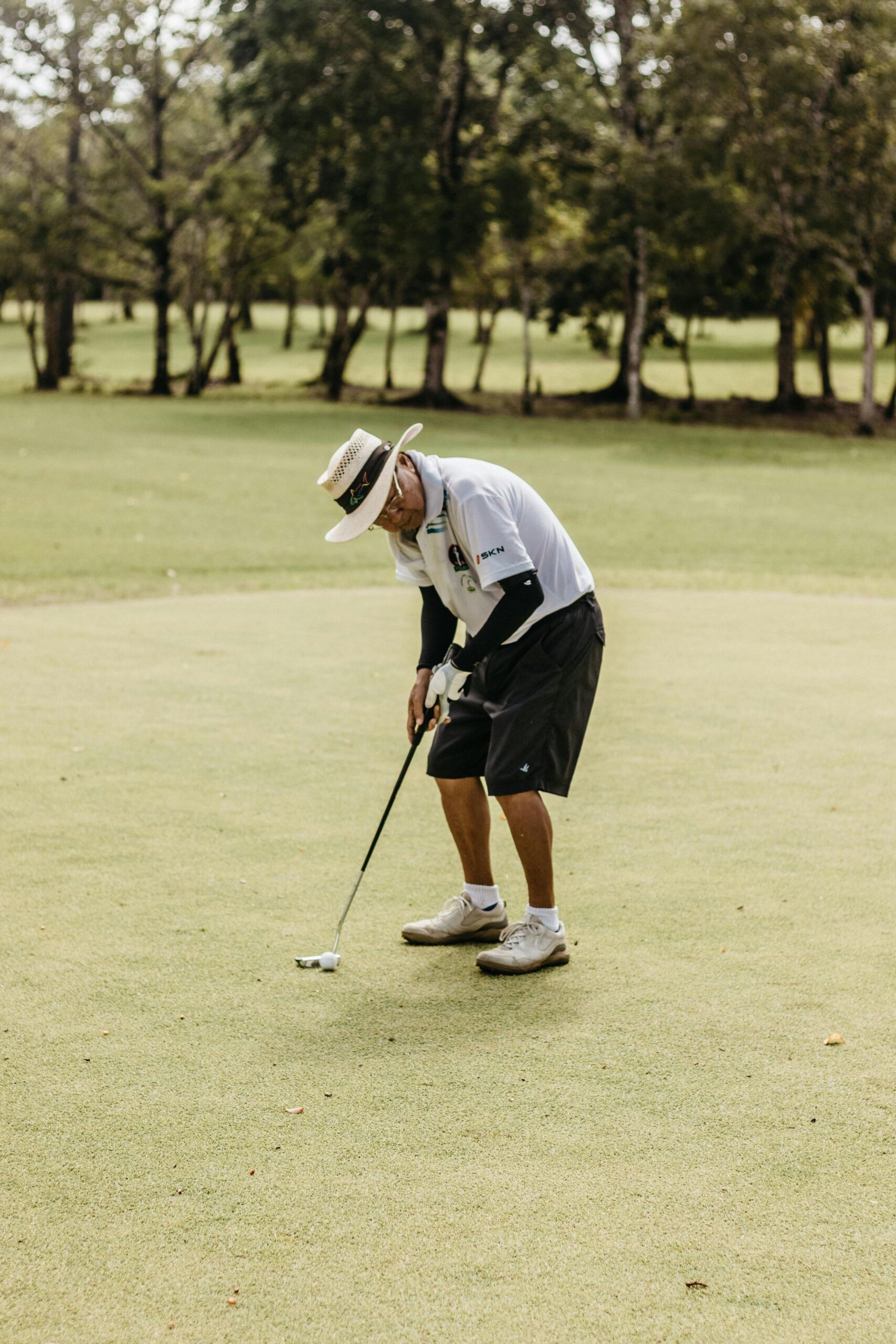 A golfer focusing on a putt on a green course on a sunny day.